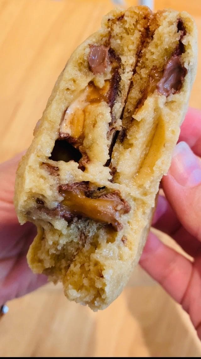 Snickers cookie torn open with molten caramel, nougat and peanut stretching